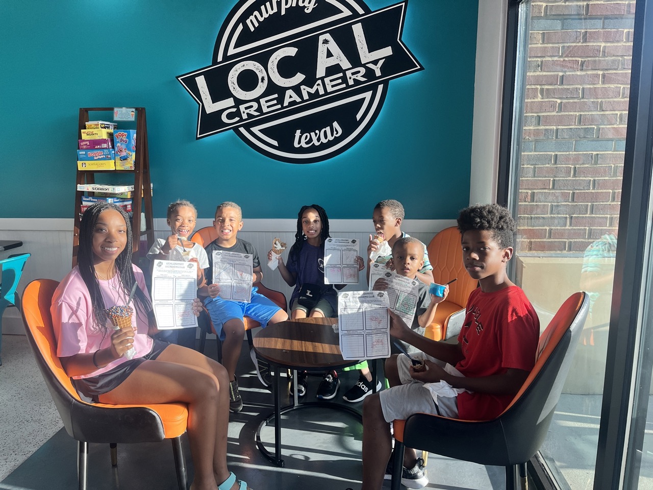 Image of kids of various ages, showing their summer reading club sheets while enjoying ice cream.