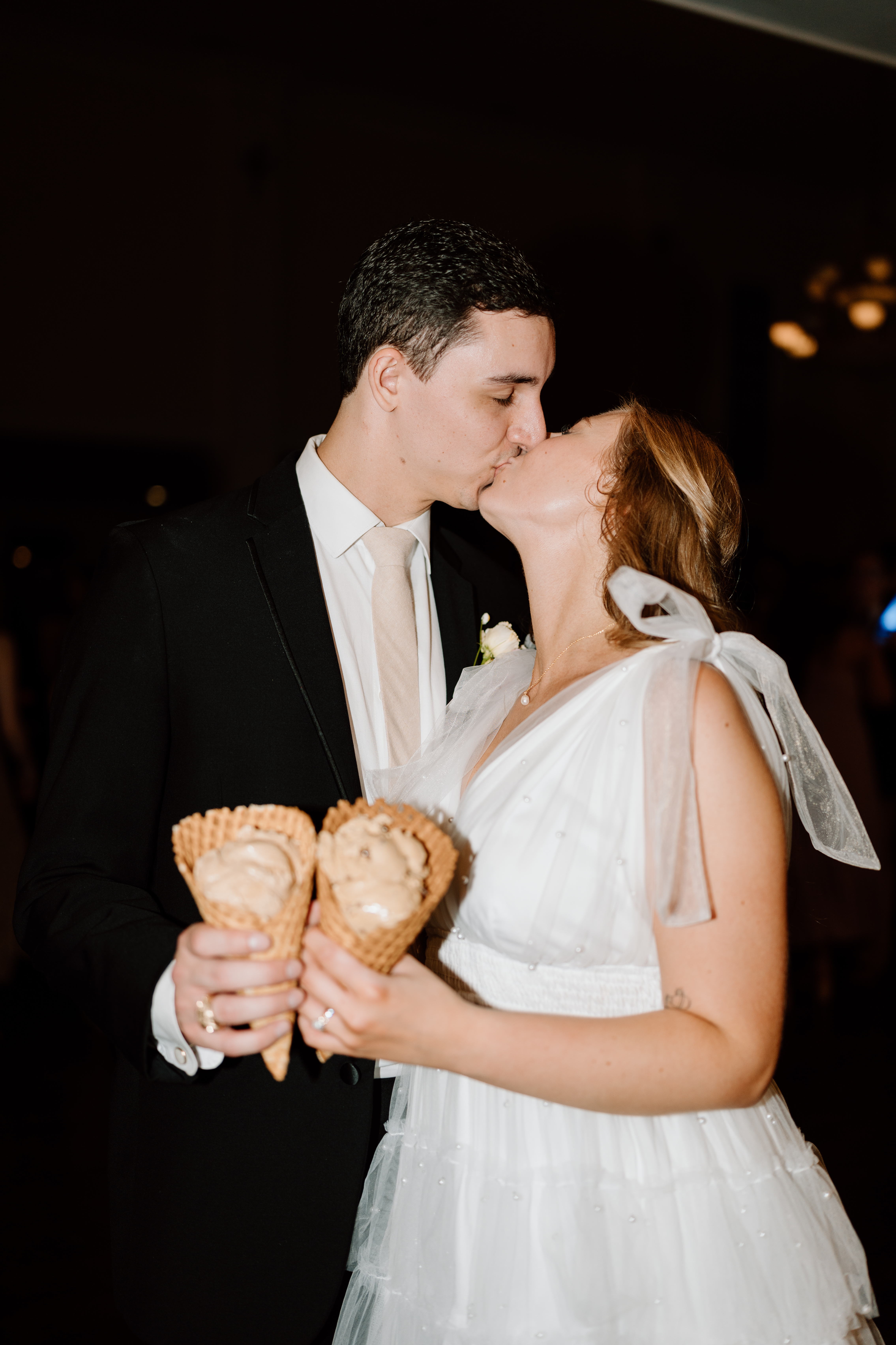 Image of a bride and groom sharing a kiss while holding ice cream cones.