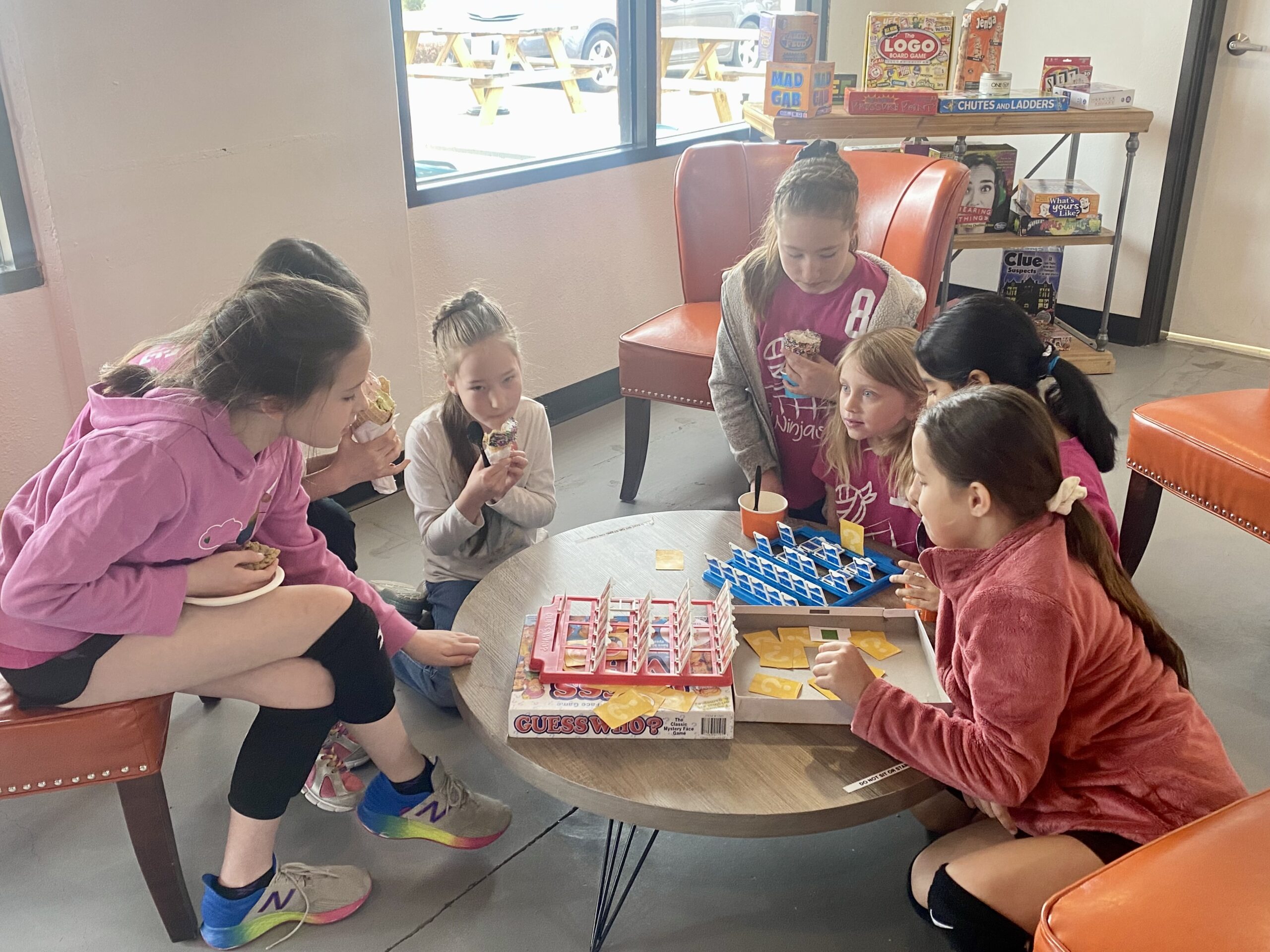 Image of kids sitting around a round table, enjoying ice cream while also playing a board game.