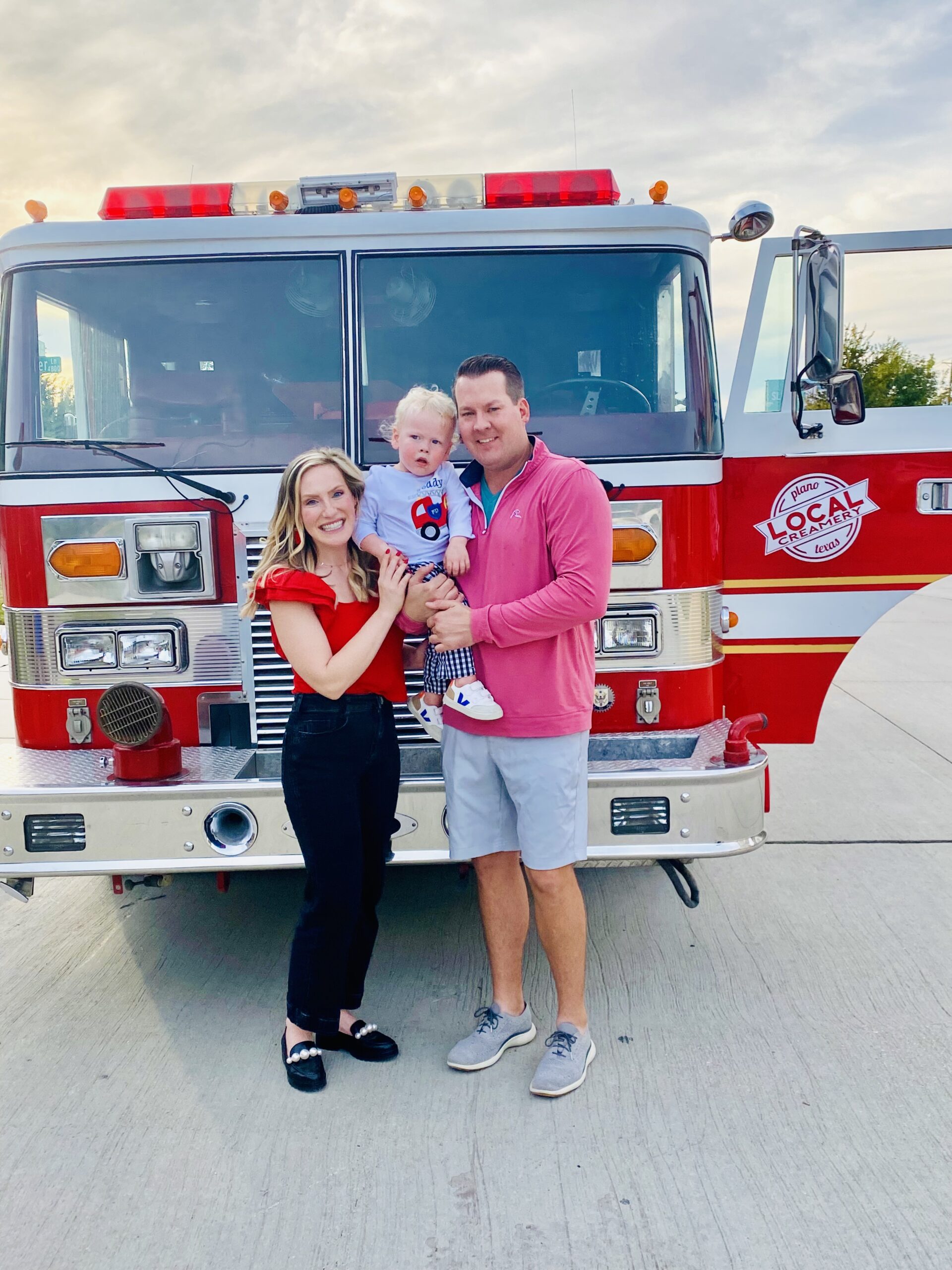 Image of a Mom and Dad smiling and holding a baby boy, while standing in front of the Local Creamery Ice Cream Fire Truck.